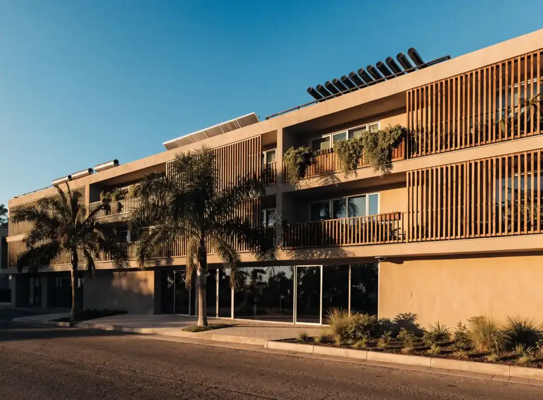 Fachada de un hotel de varios niveles con habitaciones iluminadas al atardecer